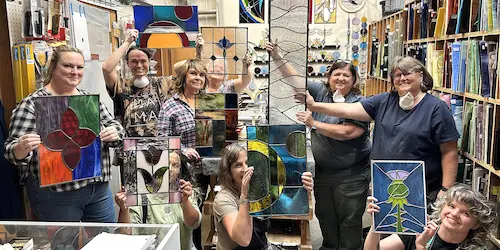 A group of people stand in a room and hold up stained glass windows